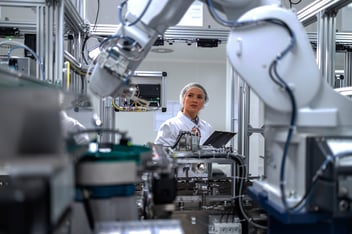Female engineer controlling production process of modern robotic arm machine in automotive industry.